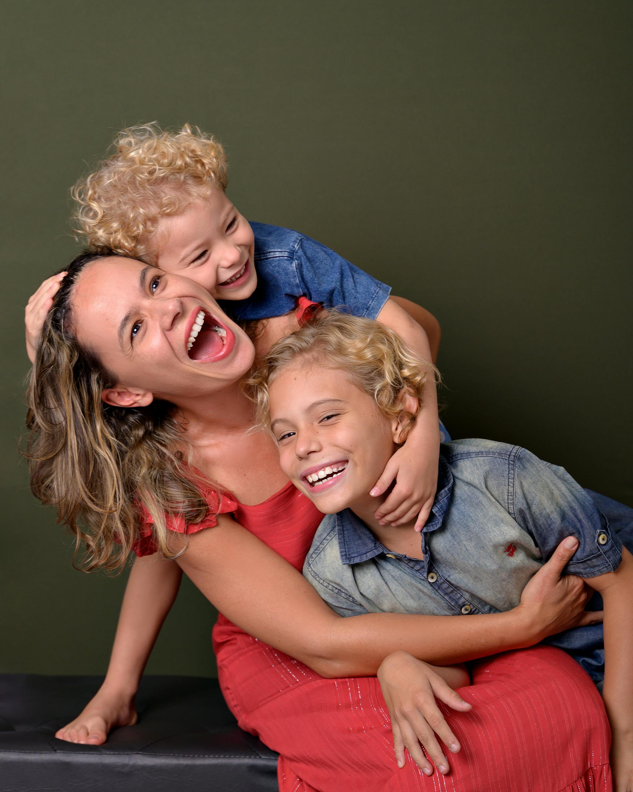 Joyful mother and her two sons laughing and hugging against a green background in a studio.