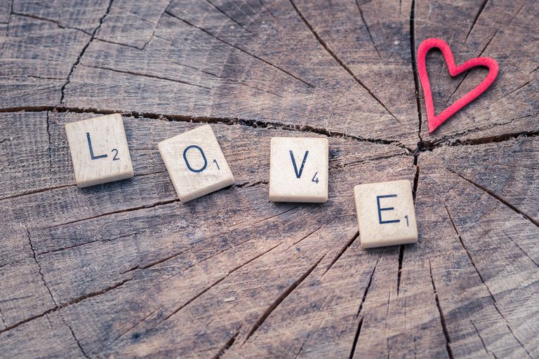 Scrabble tiles spelling 'LOVE' next to a heart shape on a wooden background.